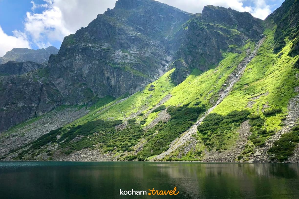 Jezioro górskie w Tatrach z zielonymi, nasłonecznionymi zboczami.