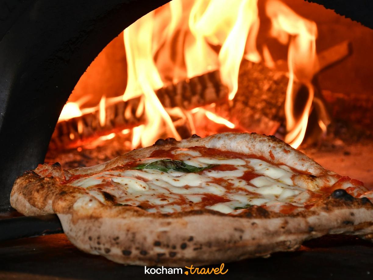 Klasyczna pizza Margherita pieczona w rozgrzanym piecu opalanym drewnem.