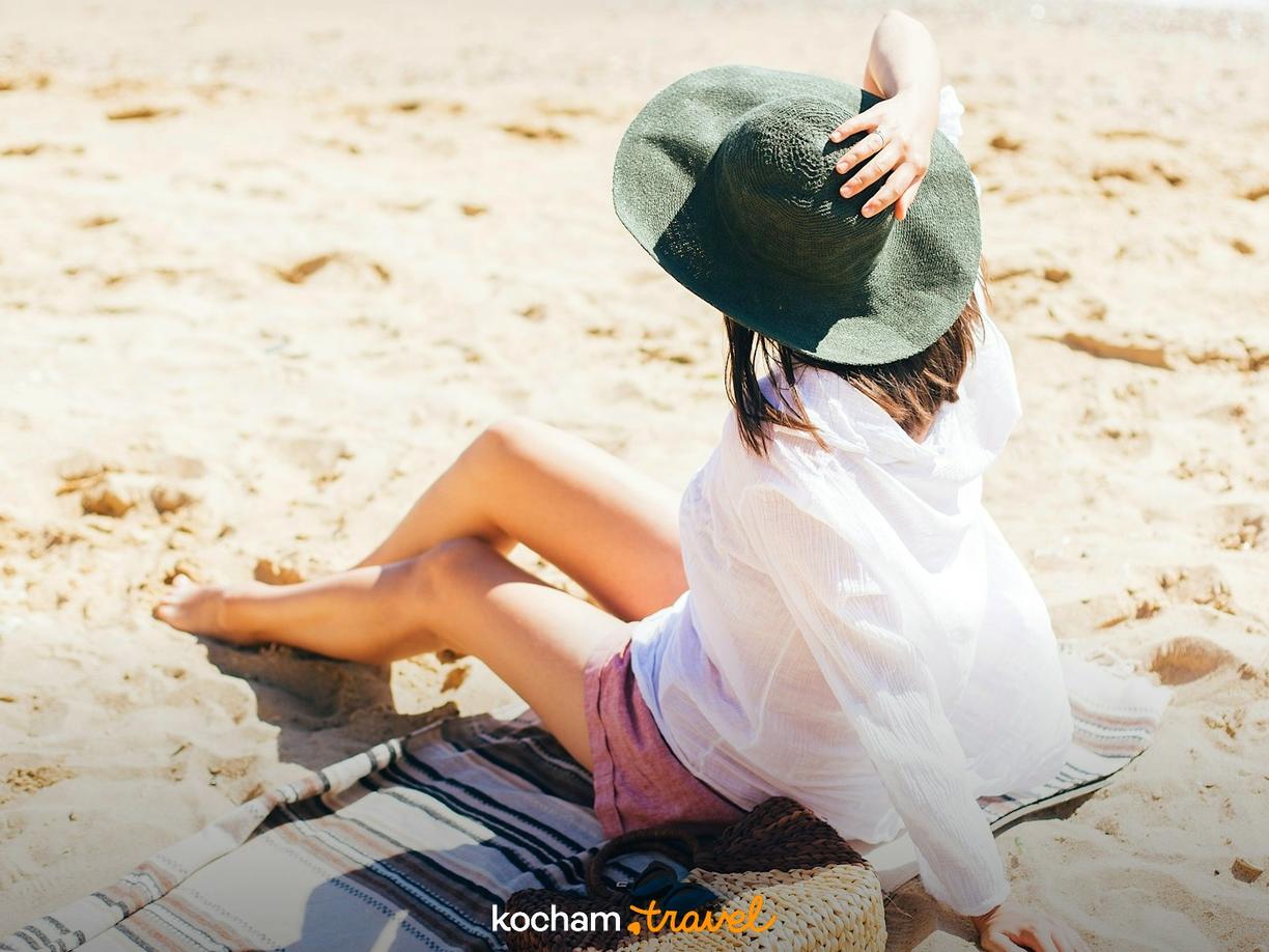 Kobieta w kapeluszu odpoczywająca na słonecznej plaży.