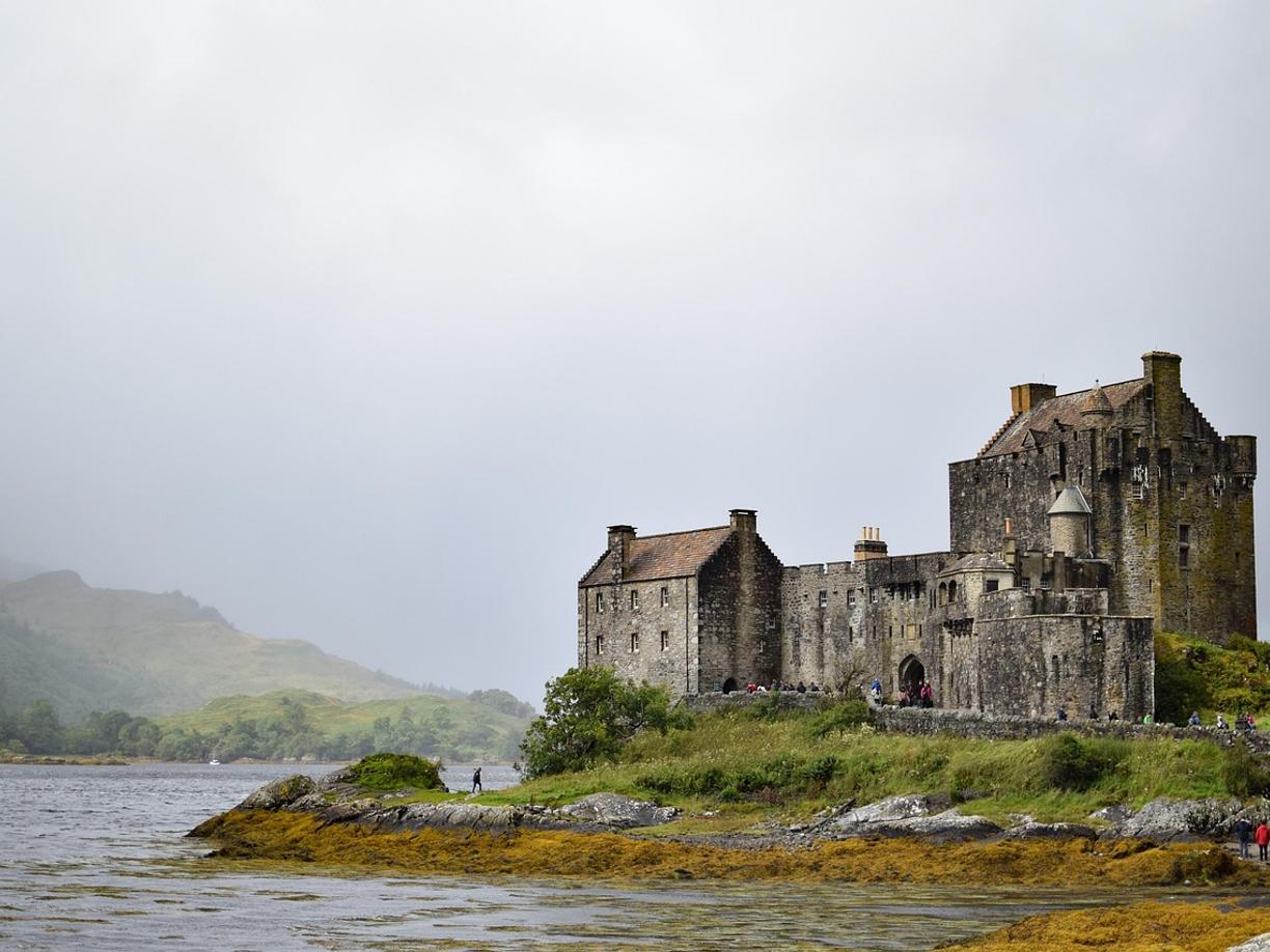Historyczny zamek Eilean Donan w Szkocji nad jeziorem, mgliste góry.