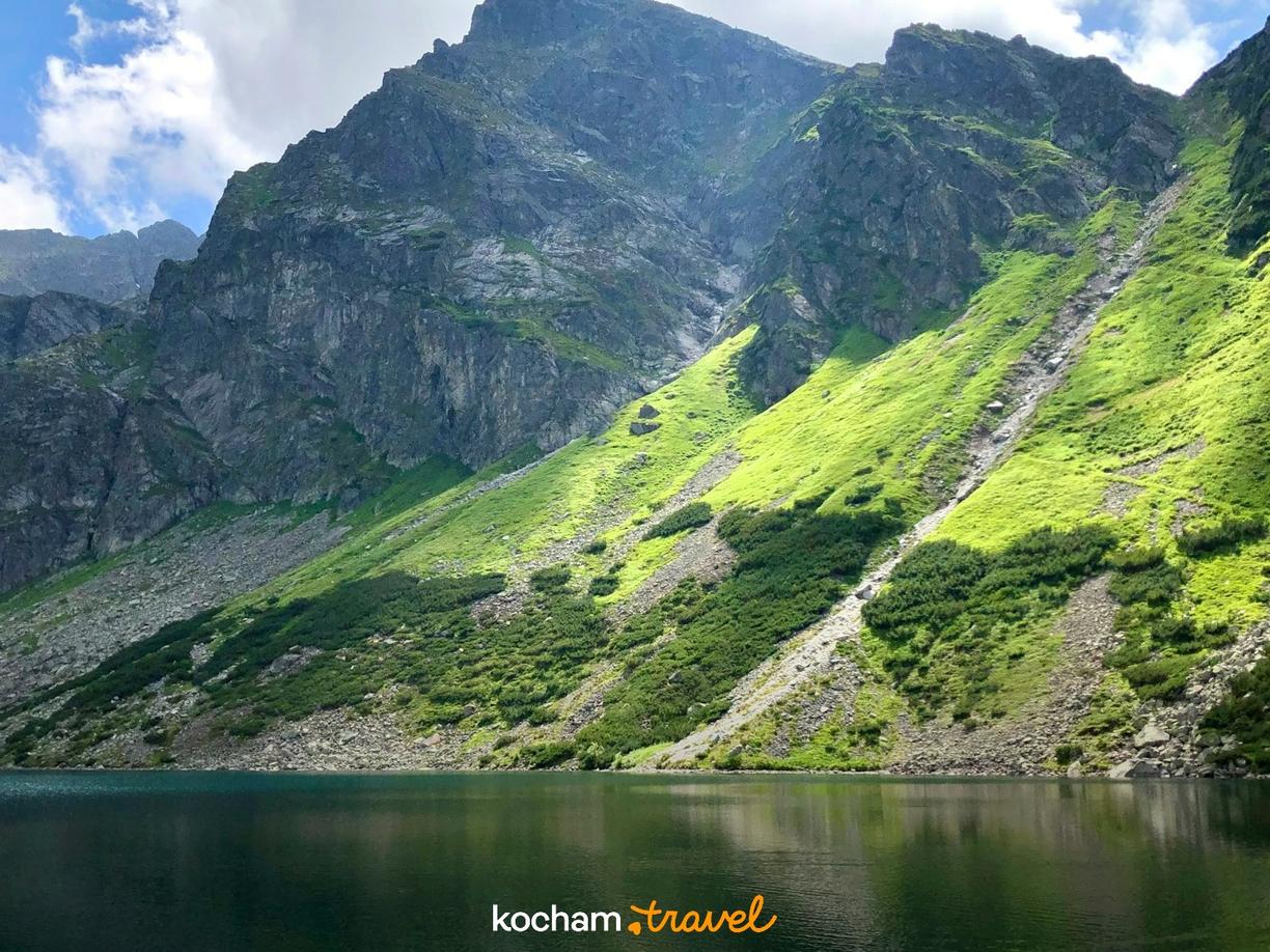 Jezioro górskie w Tatrach z zielonymi, nasłonecznionymi zboczami.