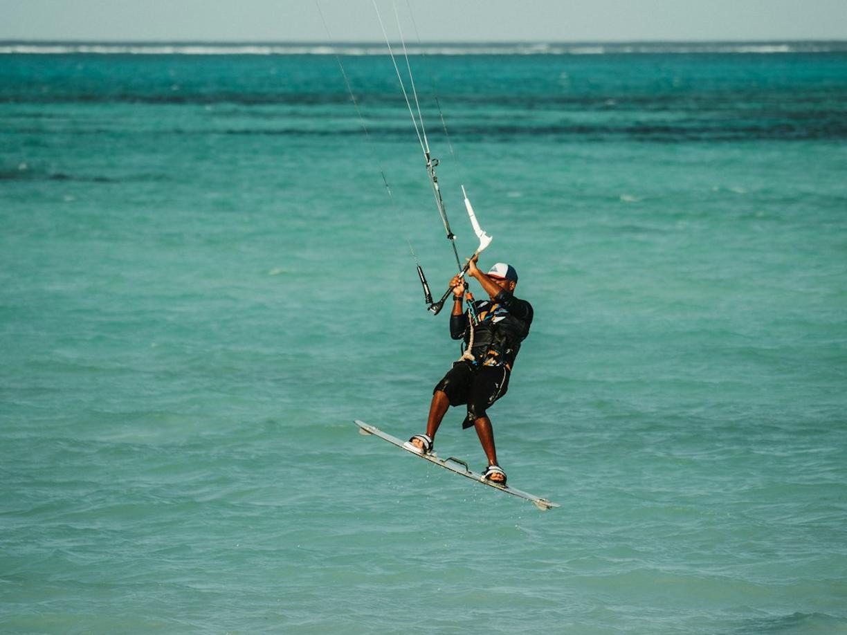 Kitesurfer w powietrzu nad turkusowym morzem i piaszczystą plażą.