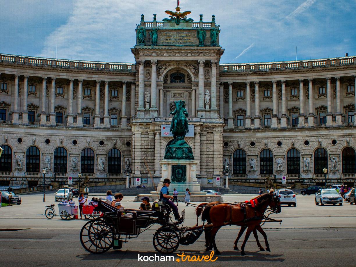 Wiedeński fiaker z turystami przed Pałacem Hofburg w słoneczny dzień.