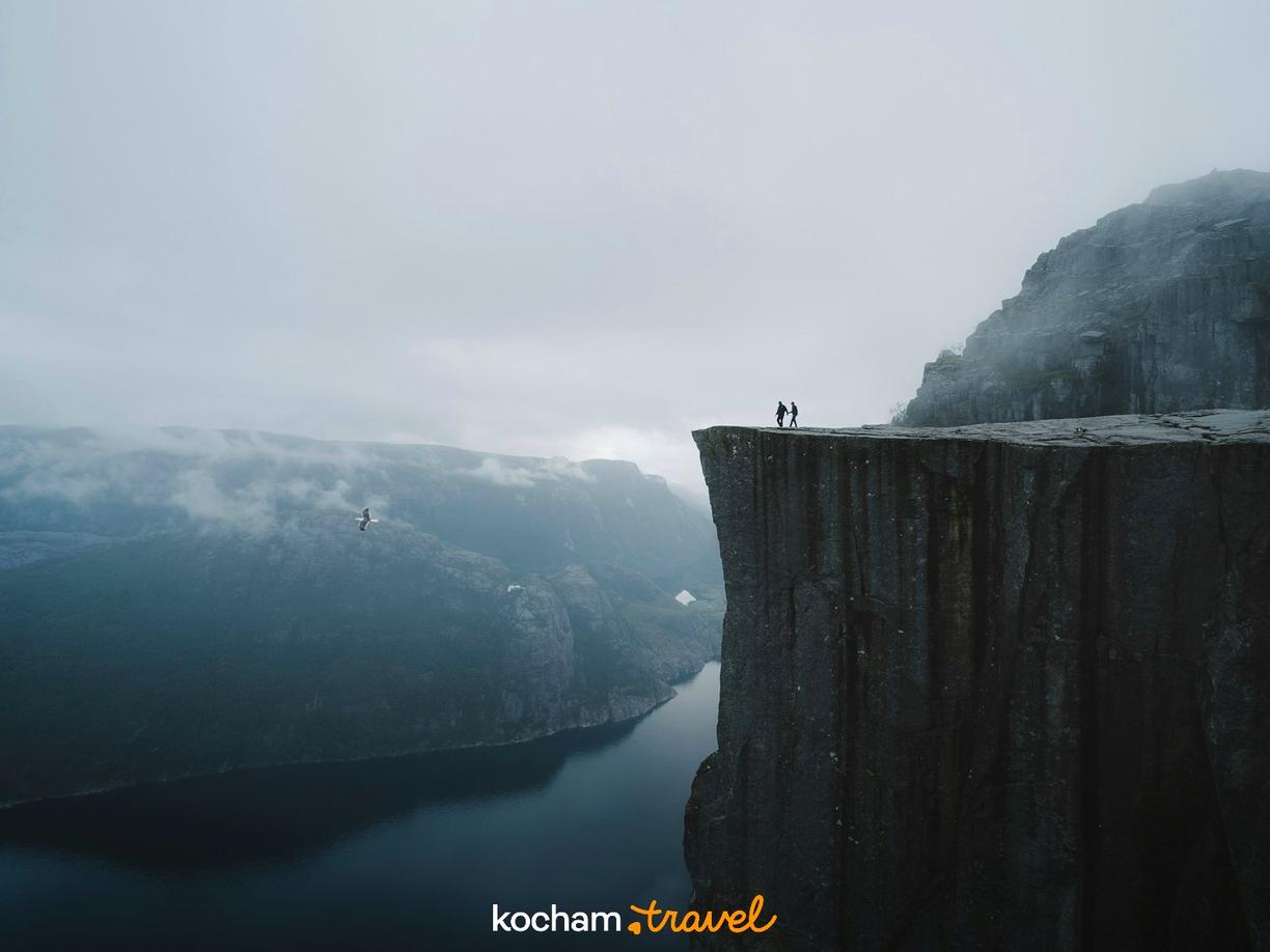 Dwoje ludzi na klifie Preikestolen, mglisty norweski fiord.