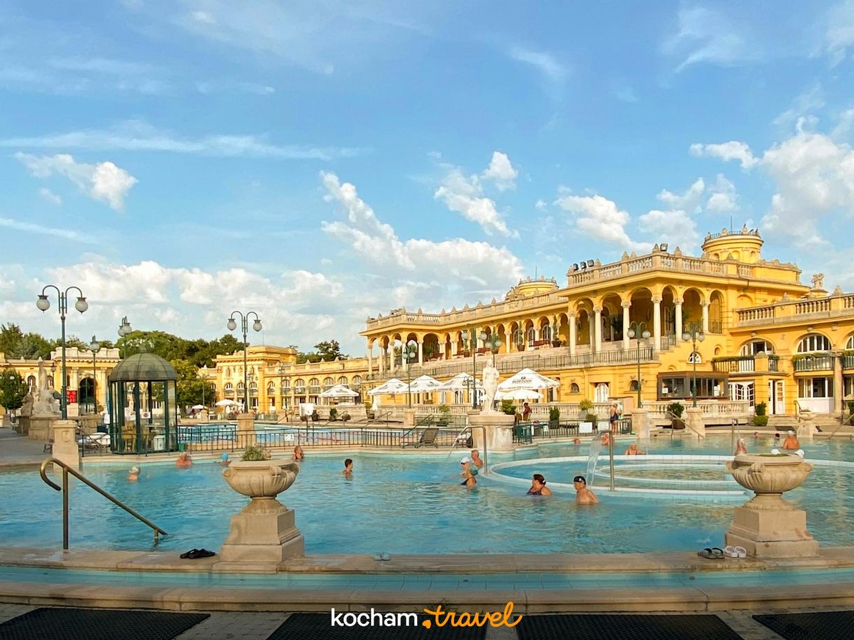Kąpielisko termalne Szechenyi w Budapeszcie, żółte budynki, relaksujący się ludzie.