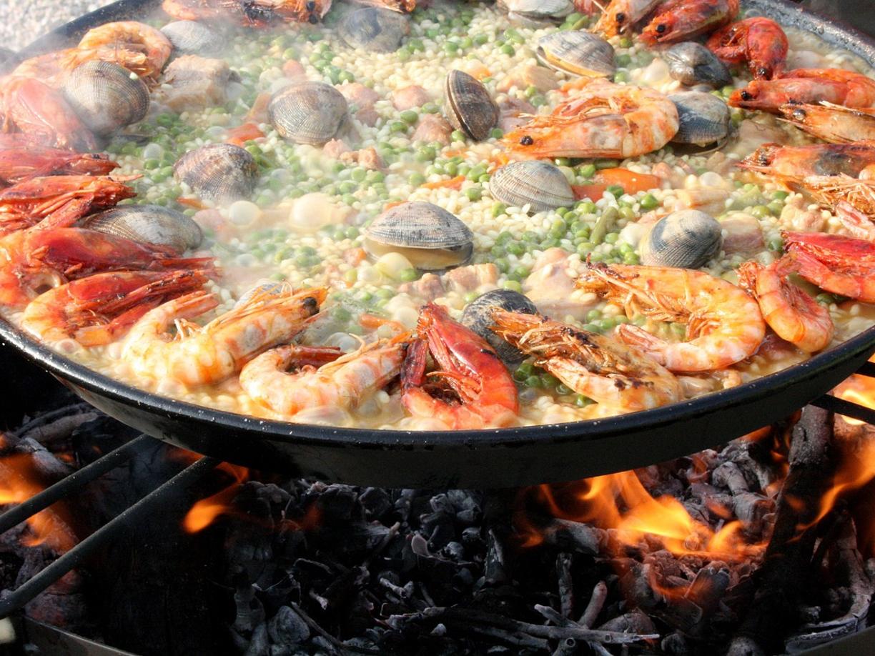 Paella z owocami morza, krewetkami i małżami gotująca się na otwartym ogniu.