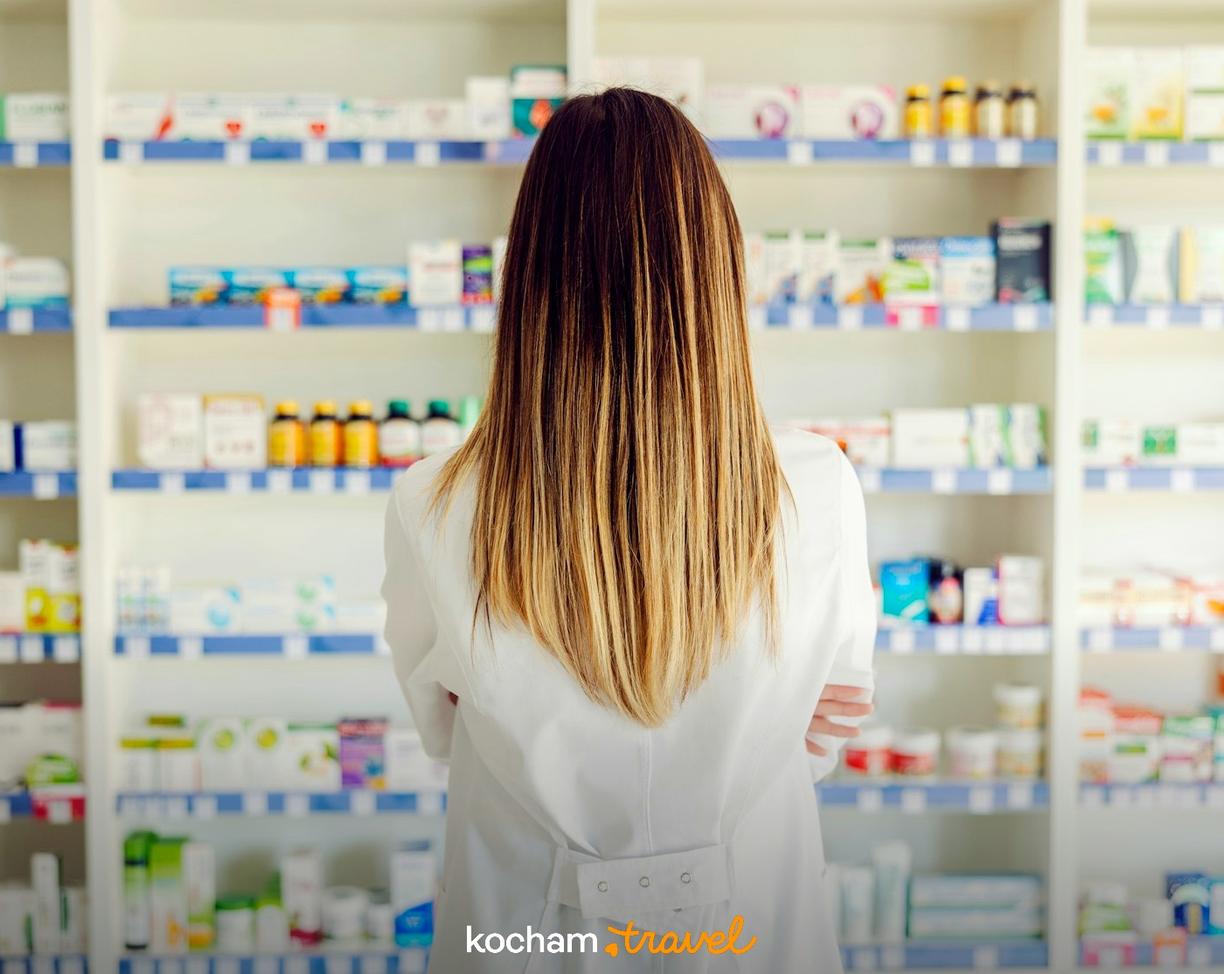 Farmaceutka stoi przed półkami pełnymi leków w aptece.