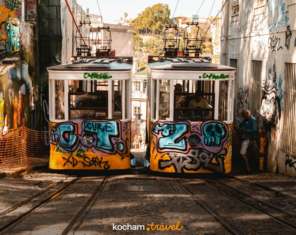 Dwa kolorowe tramwaje z graffiti na torach w słonecznej uliczce.
