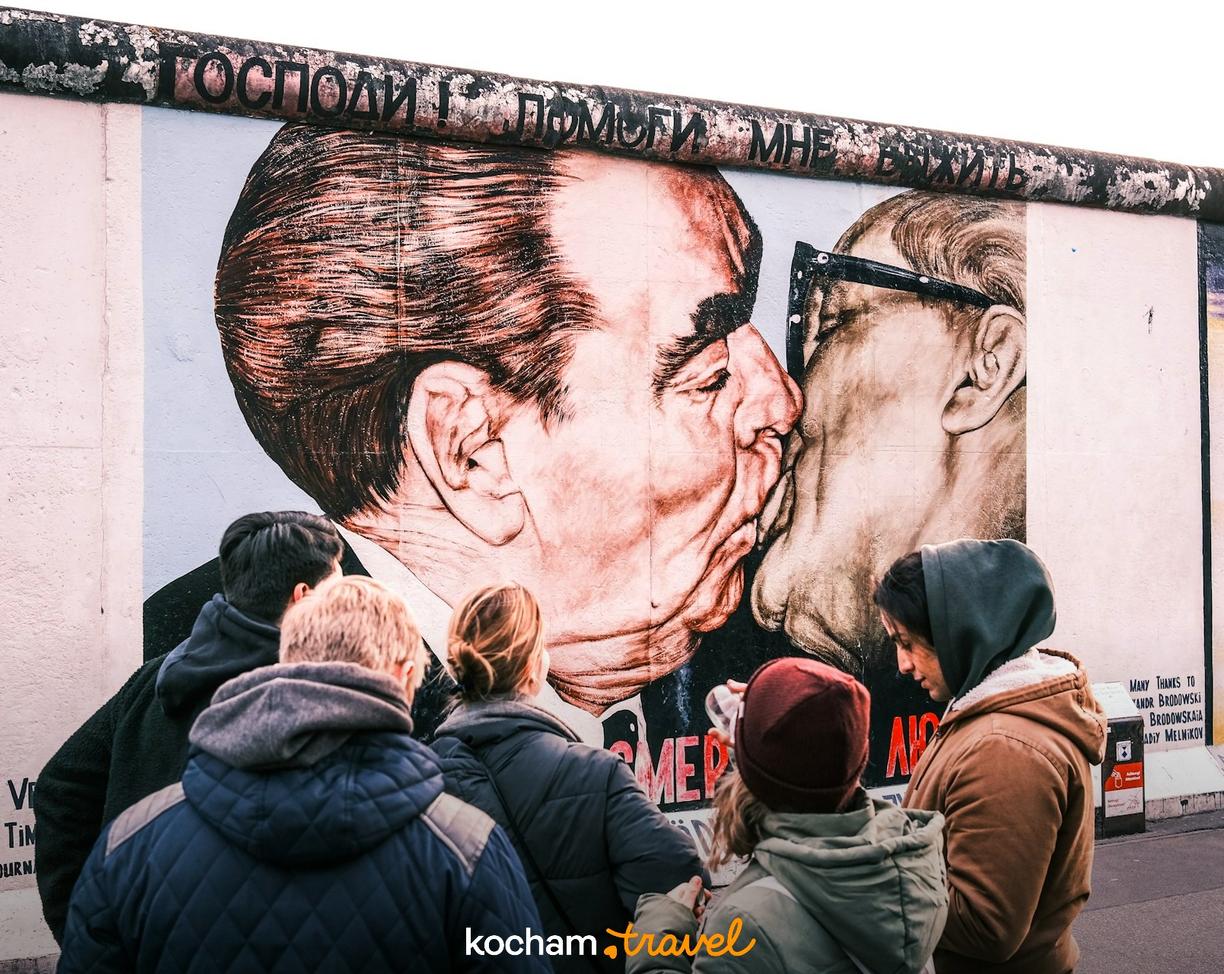 Turyści oglądają słynny pocałunek braterski na East Side Gallery w Berlinie.