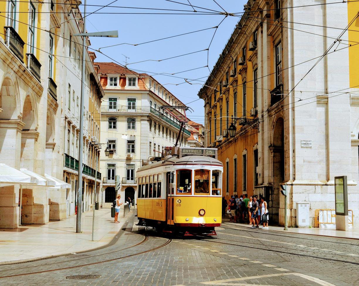 Żółty tramwaj w Lizbonie na brukowanej ulicy wśród zabytkowych kamienic.