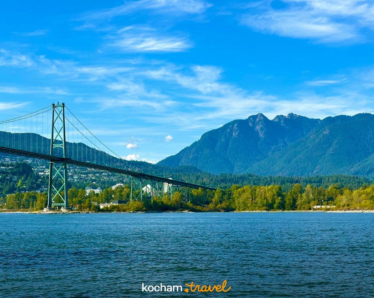 Most Lions Gate, Vancouver, błękitna woda i zalesione góry.