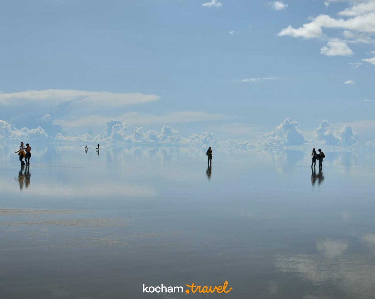 Turyści na solnisku Salar de Uyuni z idealnym odbiciem nieba.