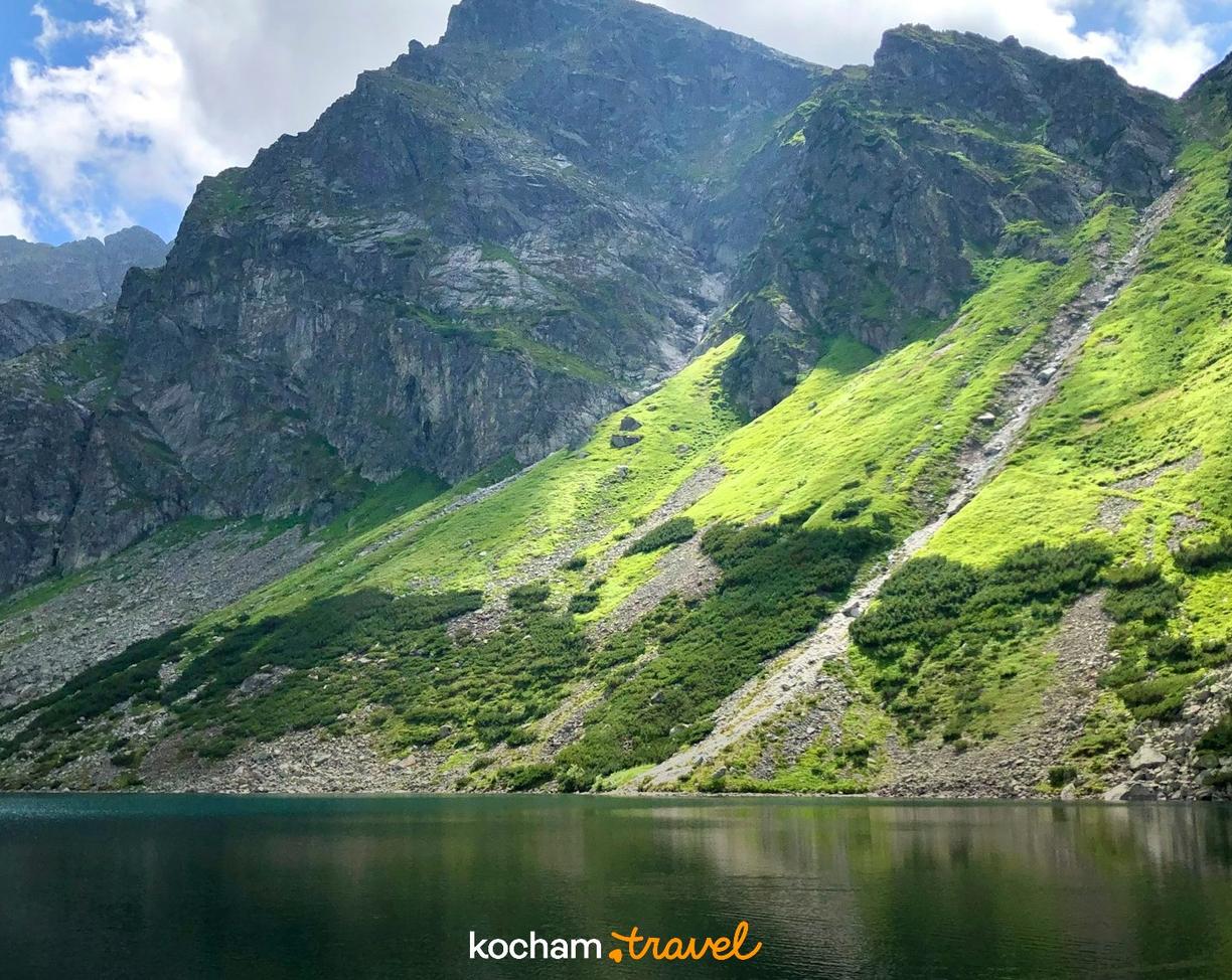 Jezioro górskie w Tatrach z zielonymi, nasłonecznionymi zboczami.