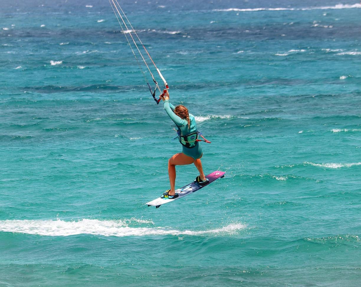 Kobieta kitesurfingowa wykonująca skok nad turkusową wodą.
