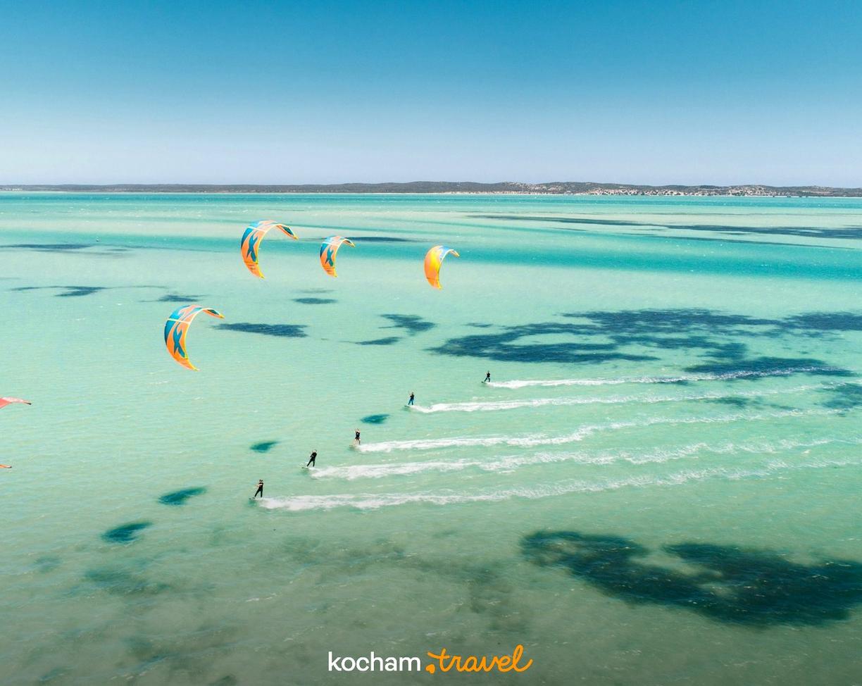 Kitesurferzy na czystej, turkusowej wodzie pod błękitnym niebem.