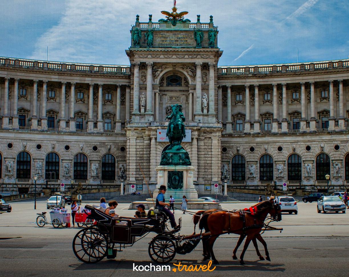 Wiedeński fiaker z turystami przed Pałacem Hofburg w słoneczny dzień.