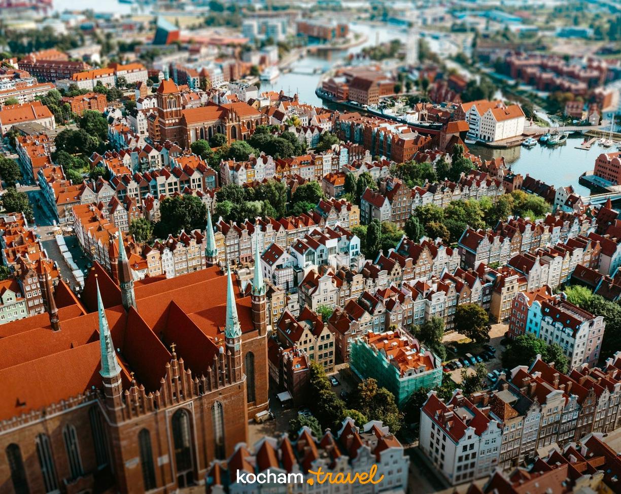 Panorama Gdańska: czerwone dachy, zabytkowe kamienice, rzeka, kościół.