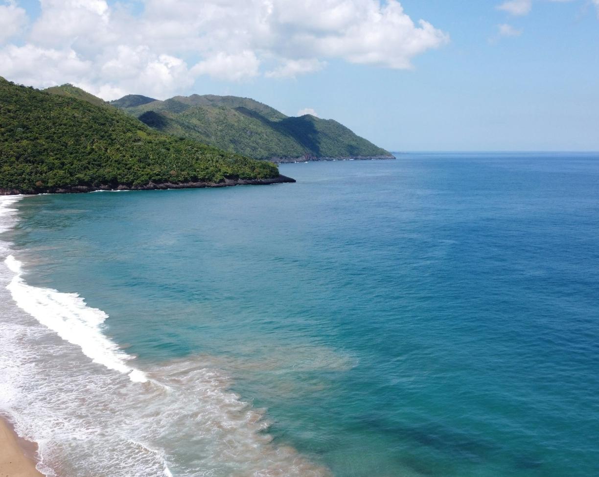 Tropikalna plaża z turkusowym oceanem, falami i zielonymi wzgórzami.