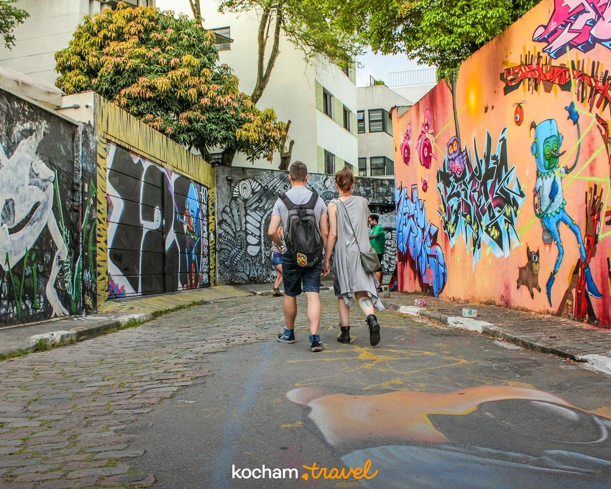 Para spacerująca brukowaną uliczką z barwnymi muralami.