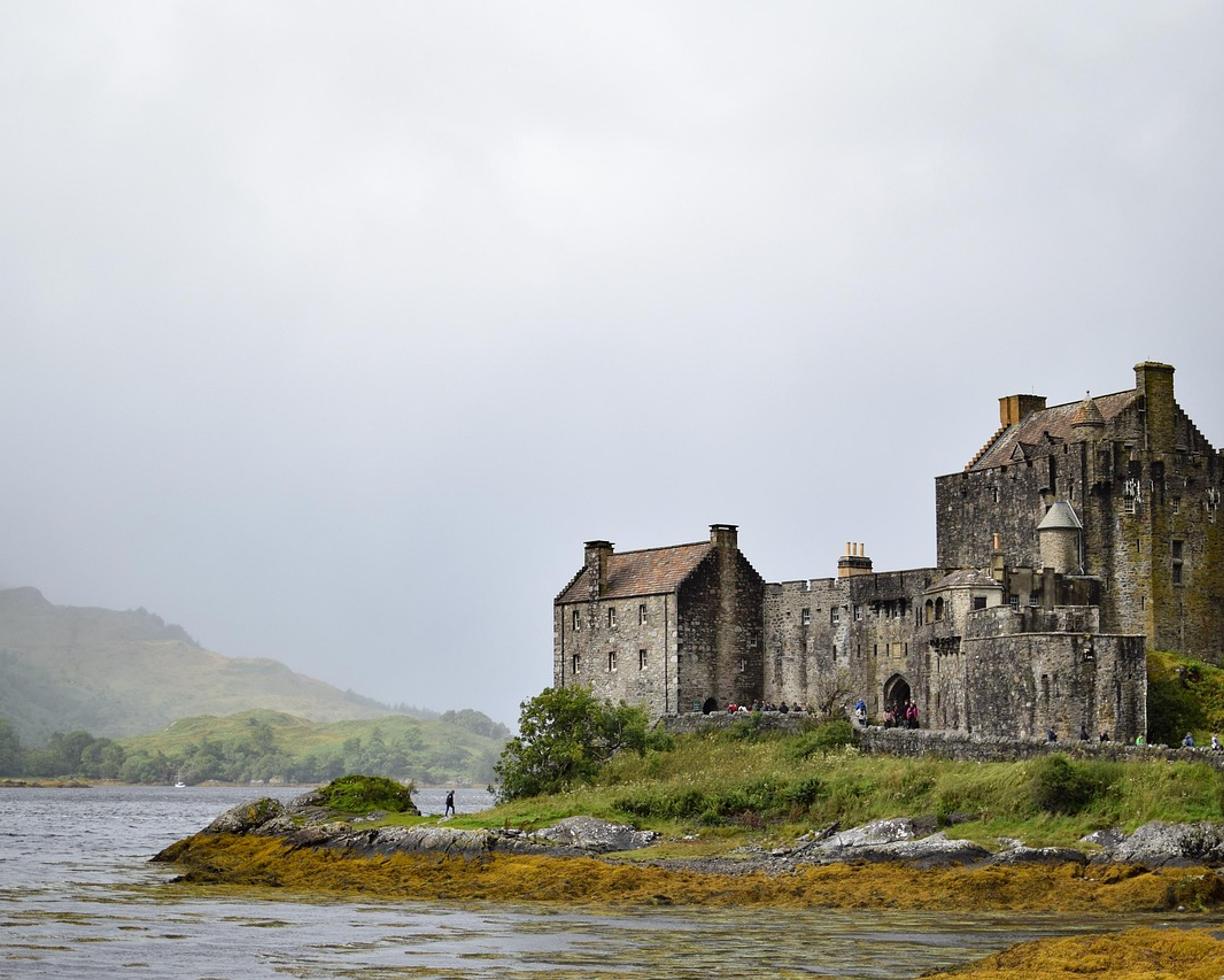 Historyczny zamek Eilean Donan w Szkocji nad jeziorem, mgliste góry.