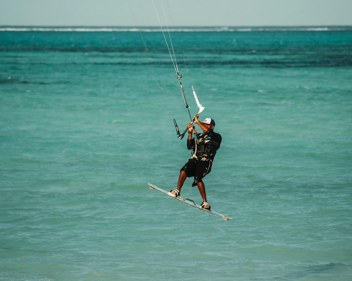 Kitesurfer w powietrzu nad turkusowym morzem i piaszczystą plażą.