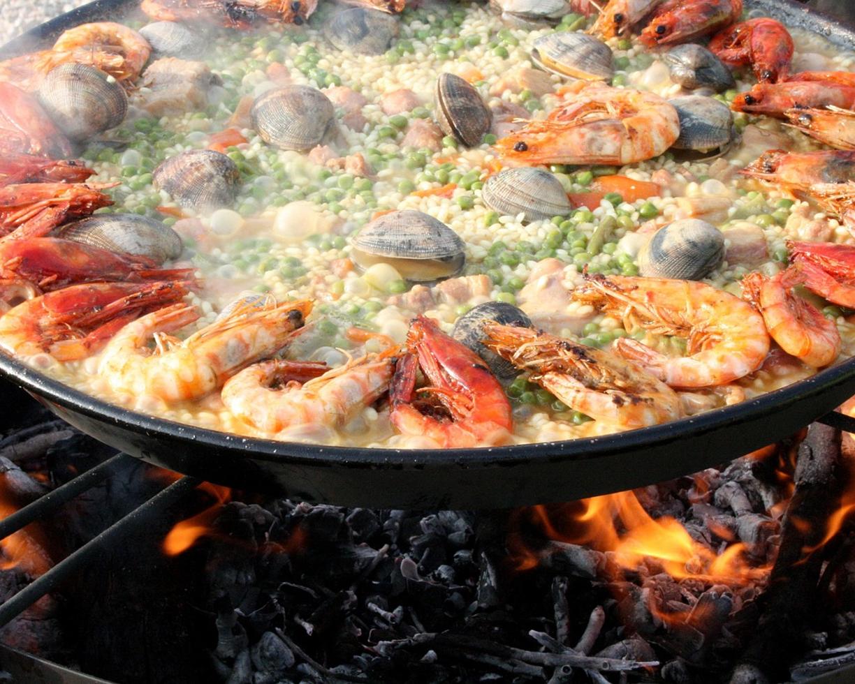 Paella z owocami morza, krewetkami i małżami gotująca się na otwartym ogniu.