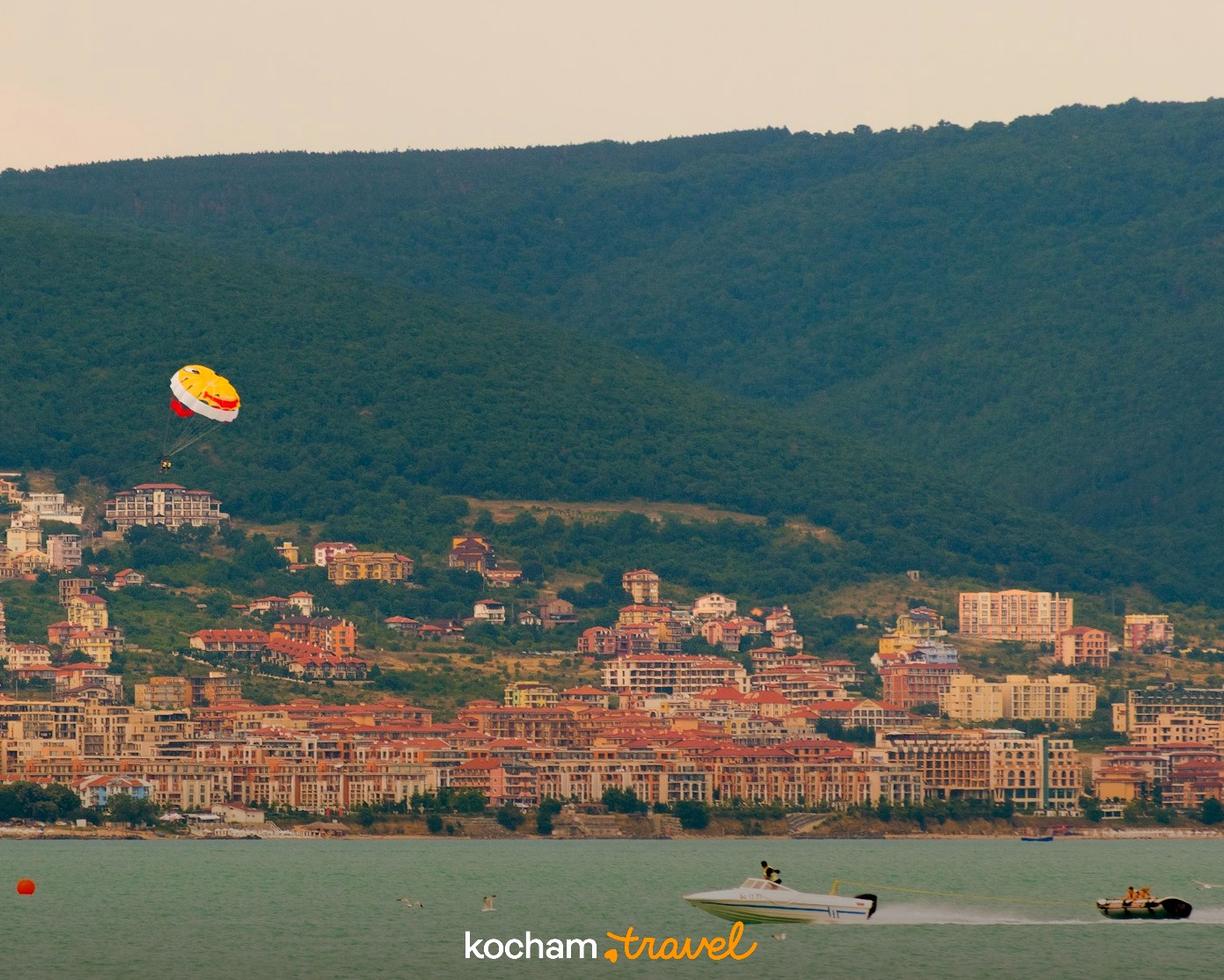 Kurort nadmorski z domami na wzgórzach, parasailing i motorówki.