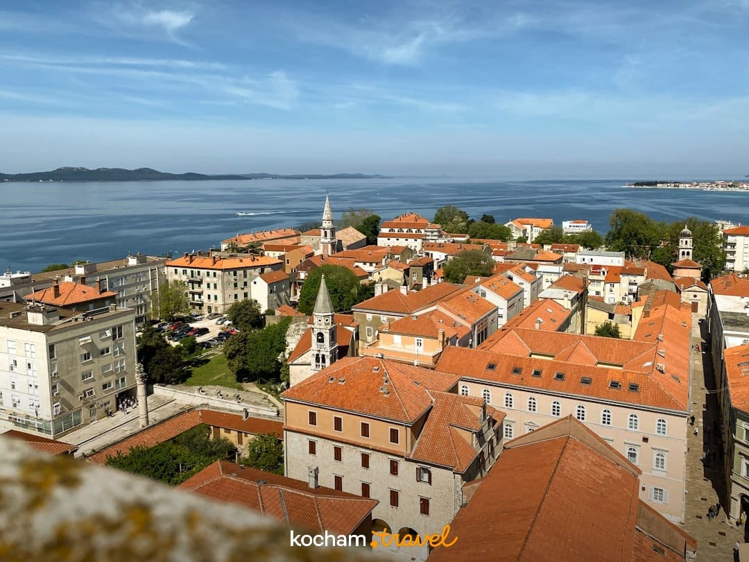 Panorama nadmorskiego miasta, czerwone dachy, błękitne morze, słoneczny dzień.