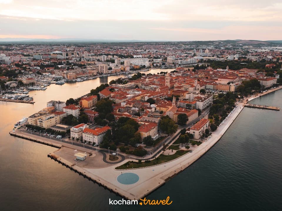 Nadmorskie miasto z czerwonymi dachami, portem i architekturą o zmierzchu.