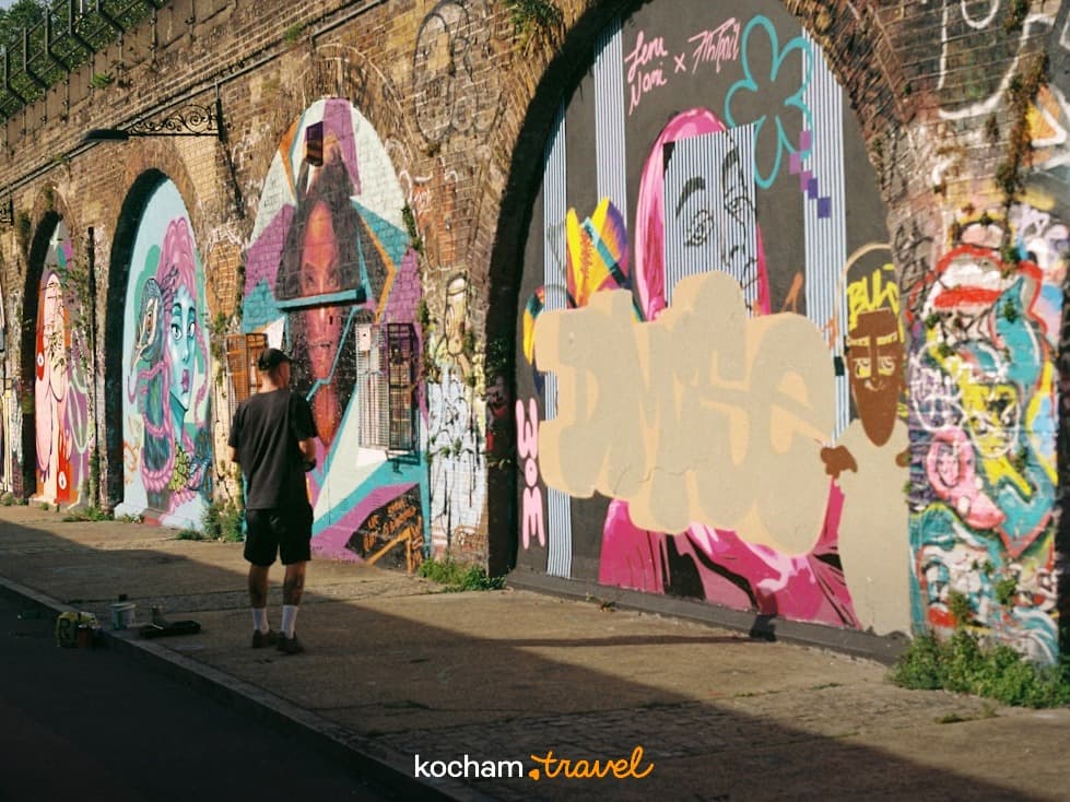 Kolorowe graffiti na łukach miejskiego wiaduktu, osoba na chodniku.