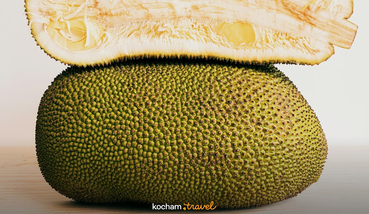 Jackfruit przekrojony, ukazujący zieloną kolczastą skórkę i jasnożółty miąższ.