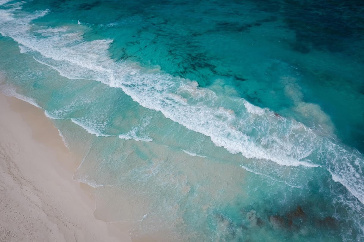 Turkusowe fale oceanu rozbijające się o piaszczystą plażę.