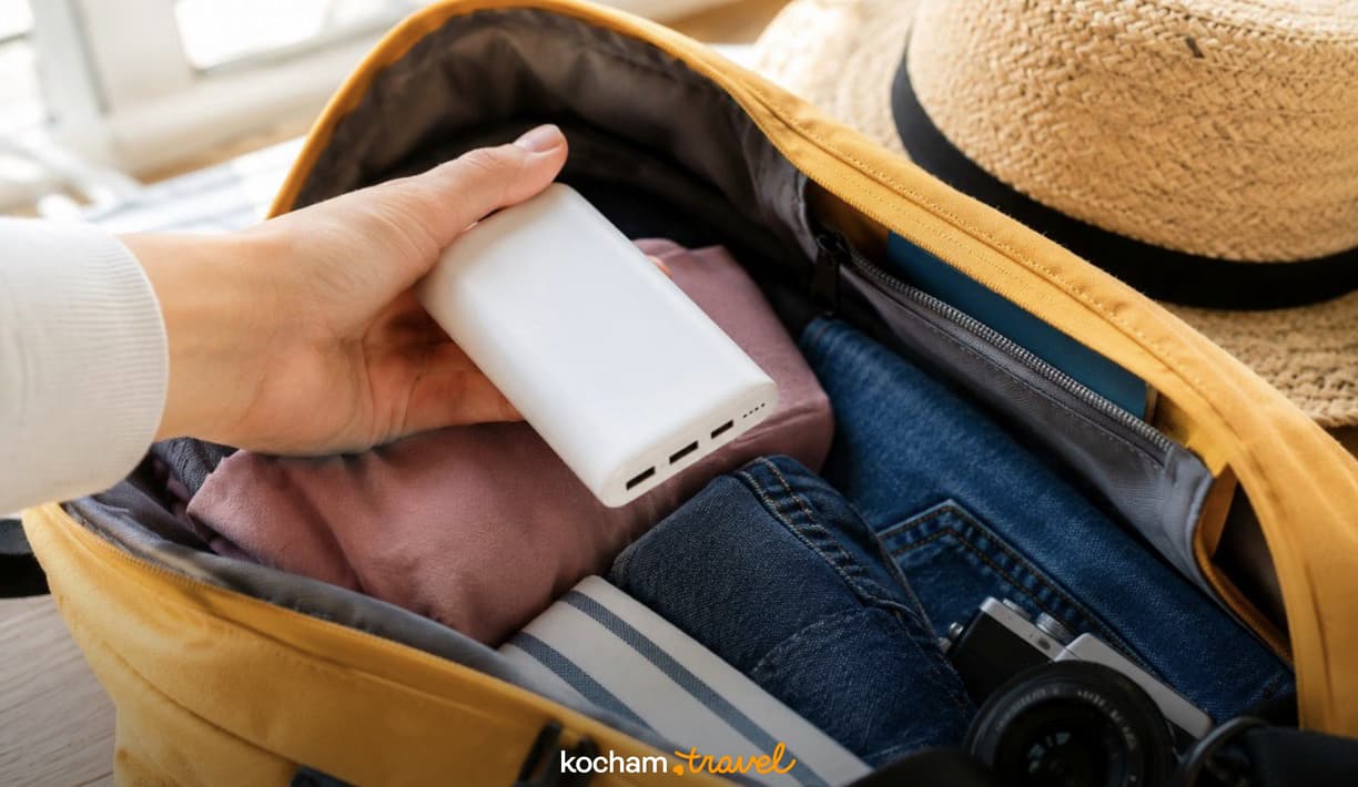 Ręka wkłada power bank do wypełnionej walizki podróżnej z ubraniami.