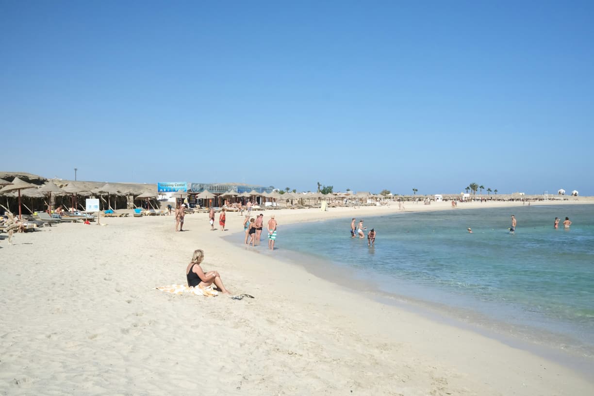 Słoneczna plaża z białym piaskiem i turkusową wodą, pełna ludzi.