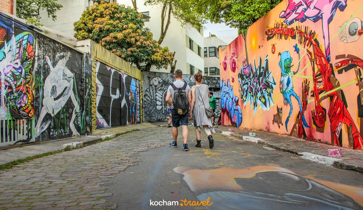 Para spacerująca brukowaną uliczką z barwnymi muralami.
