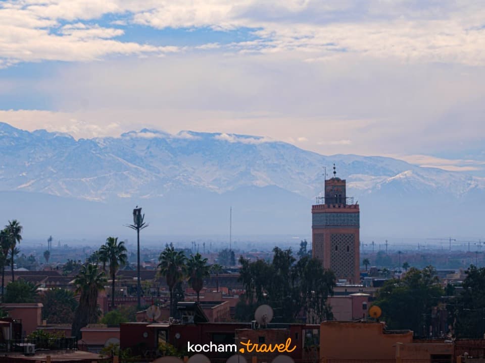 Panorama Marrakeszu z minaretem i ośnieżonymi górami Atlas w tle.