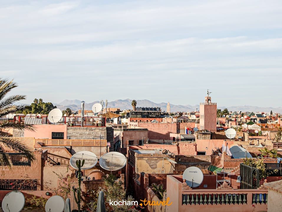 Panoramiczny widok na dachy Marrakeszu, minaret, anteny satelitarne, góry.