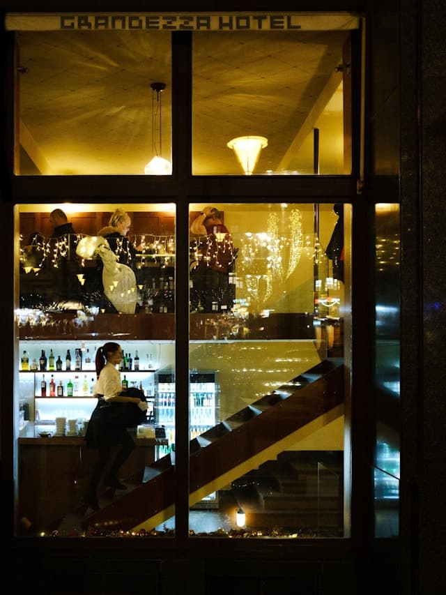 Oświetlone wnętrze baru Grandezza Hotel z ludźmi i schodami.