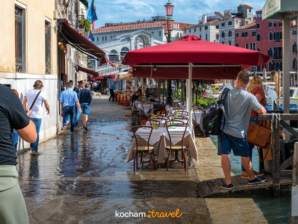 Wenecja, zalana ulica, turyści, restauracje, Most Rialto, słoneczny dzień.