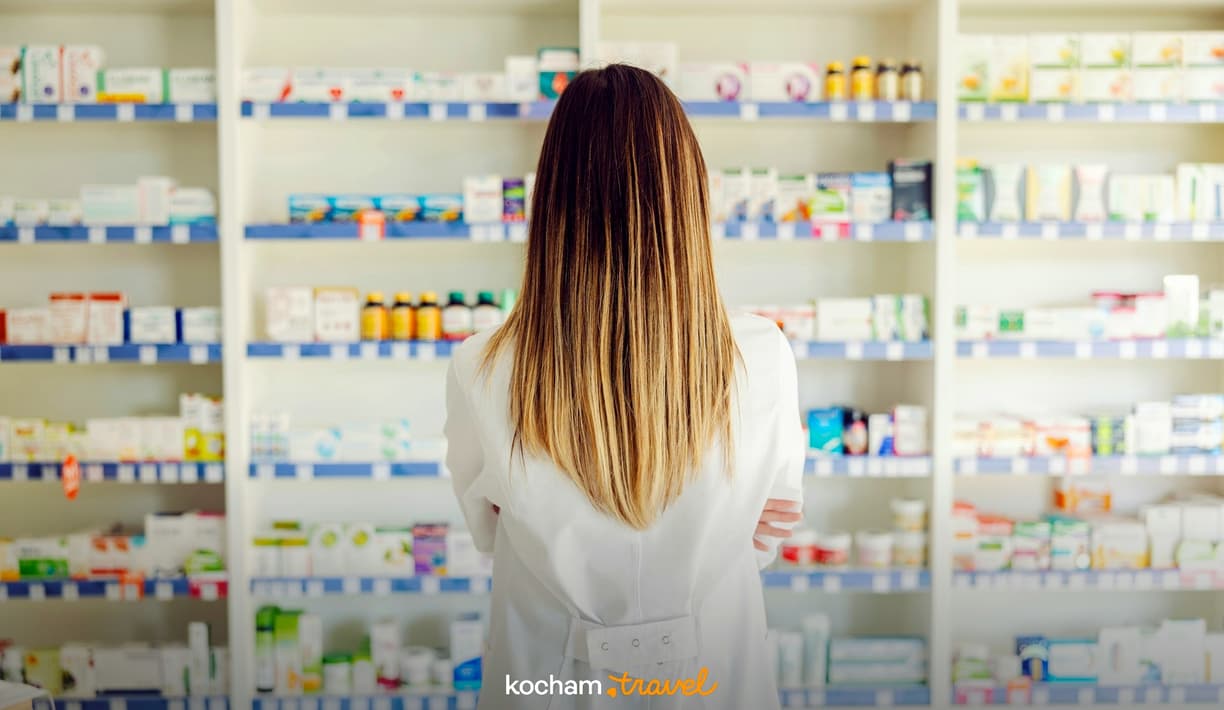 Farmaceutka stoi przed półkami pełnymi leków w aptece.