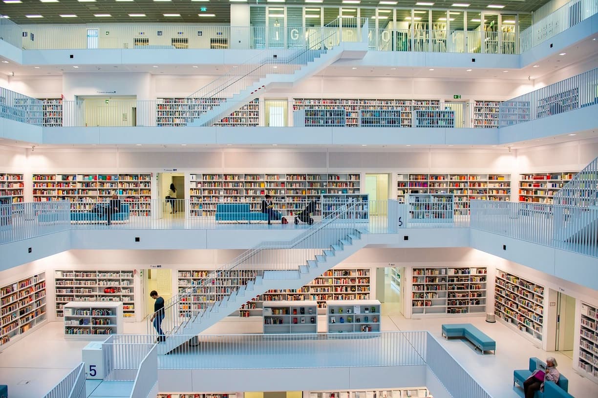 Nowoczesne wnętrze biblioteki, białe regały z książkami, ludzie, jasne schody.