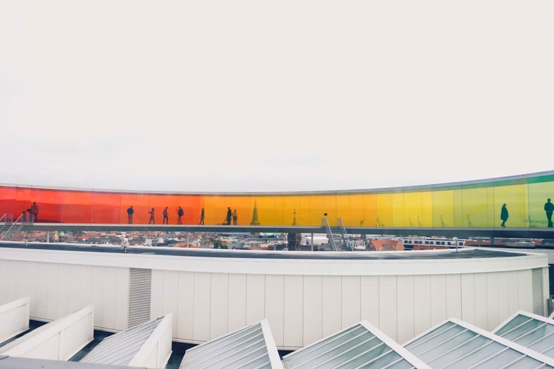 Tęczowa instalacja artystyczna na dachu, ludzie spacerujący, widok na miasto.
