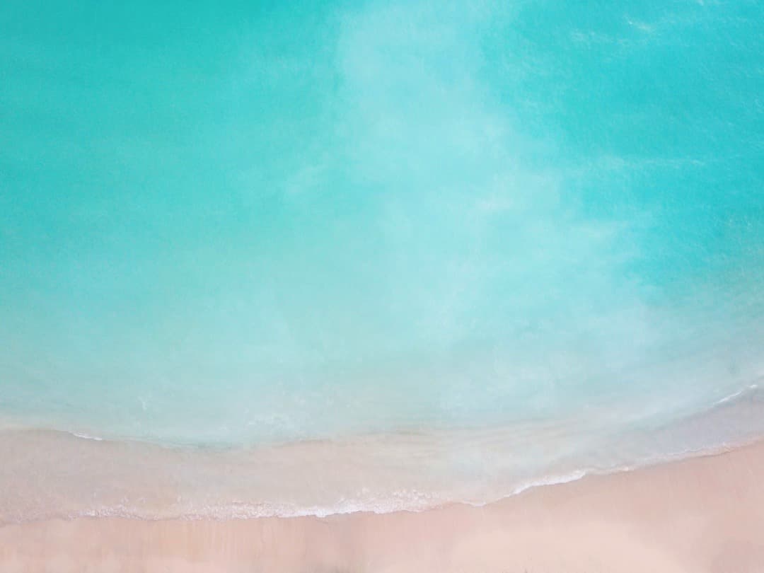 Turkusowa woda oceanu, piaszczysta plaża, delikatne fale, widok z góry.