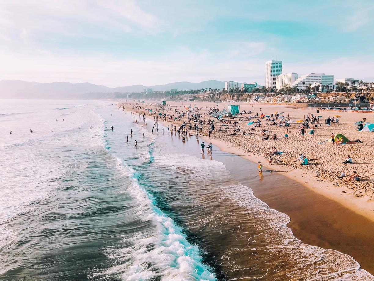 Tłoczna plaża z falującym oceanem i miastem w tle.