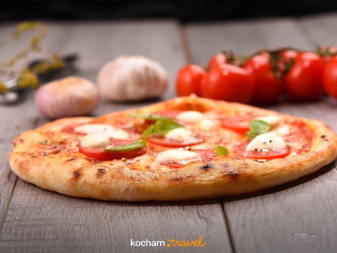 Pizza Margherita ze świeżymi pomidorami, mozzarellą i bazylią na drewnianym stole.