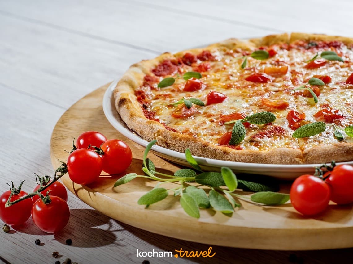 Pizza Margherita z serem, pomidorkami koktajlowymi i świeżymi ziołami na desce.