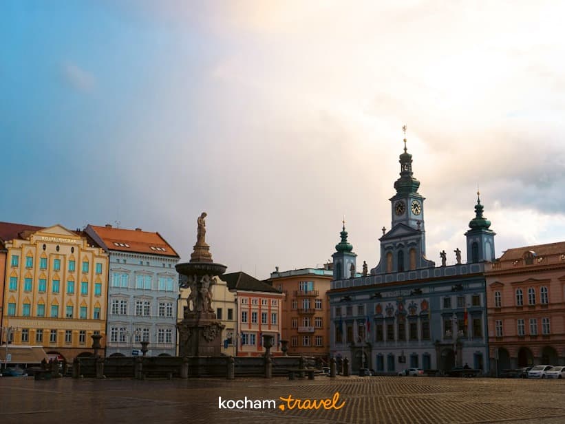 Europejski rynek z barokową architekturą, wieżą zegarową i fontanną.