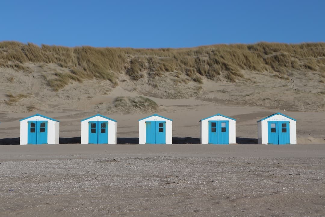 Białe domki plażowe z niebieskimi drzwiami na plaży