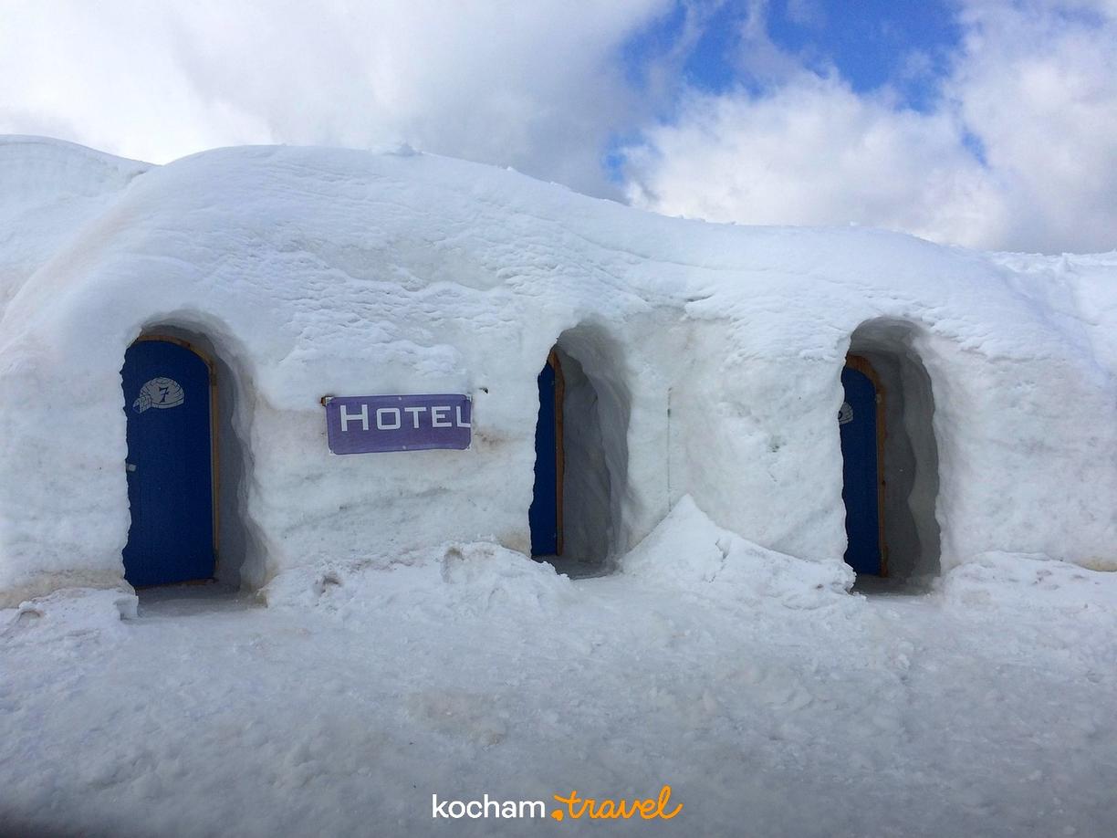 Hotel ze śniegu z niebieskimi drzwiami, zimowy krajobraz.