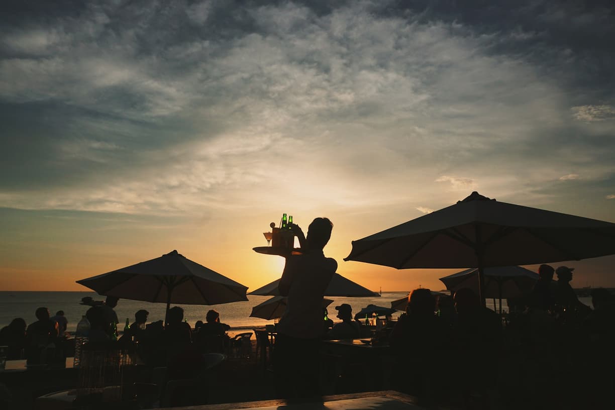 Plażowy bar o zachodzie słońca, kelner serwuje drinki gościom.